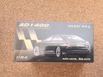 A 1:64 scale model car box for the Audi A6 (C8) / A6 (C8B), featuring a black car graphic and gold text, placed on a brown textured surface.