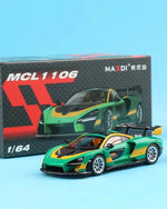 A 1/64 scale model toy car of a green, black, and yellow sports car, shown in front of its black and red retail packaging box on a light blue background.