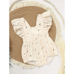 Beige baby romper with ruffled details on a textured mat