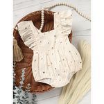 Beige baby romper with ruffled details on a wooden surface with decorative elements.
