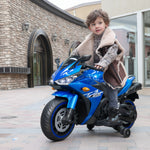 Toddler boy riding a blue electric toy motorcycle on a paved walkway.