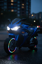 Blue electric kids ride-on motorcycle with glowing LED wheels at night