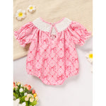 Pink baby romper with bow pattern on a textured surface with flowers.