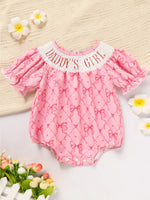 Pink baby romper with 'Daddy's Girl' text on a textured surface with flowers.
