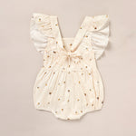 White baby romper with gold embellishments on a beige background