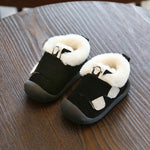 Pair of black baby booties with white faux fur trim and adjustable straps on a wooden table